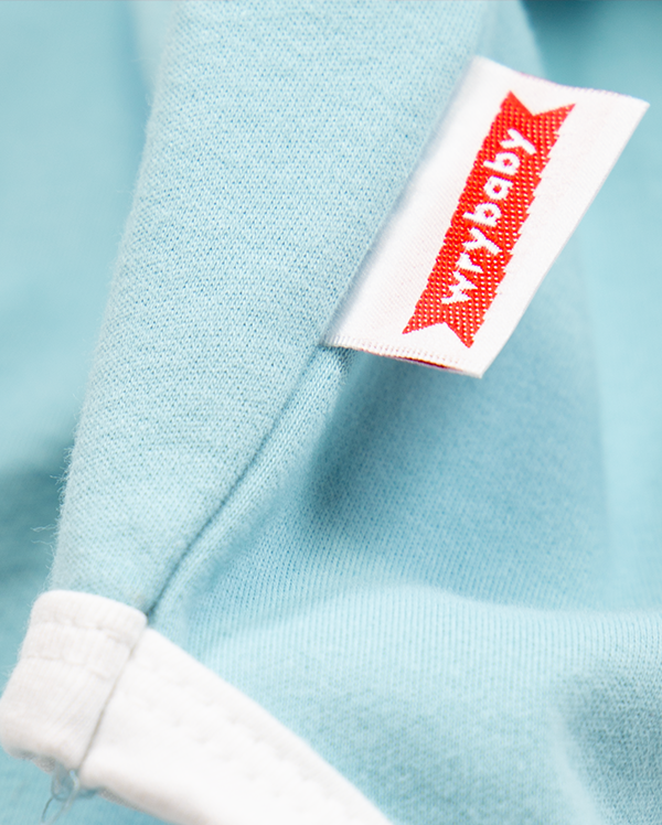 Close up of wrybaby's funny 'I Identify as a Baby' onesie showing the baby bodysuit's decorative woven label sewn at the hip
