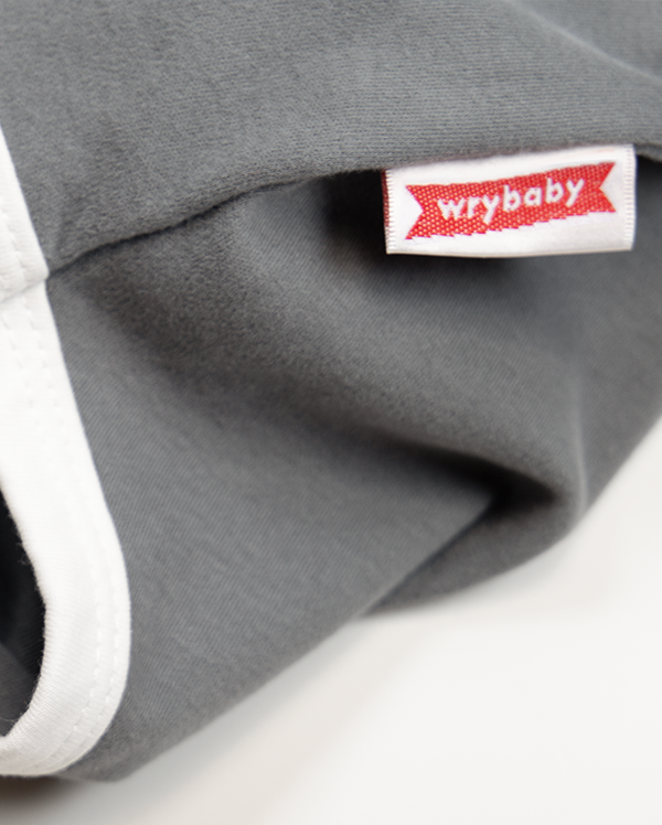 Close up of wrybaby's funny 'Expensive AF' onesie showing the baby bodysuit's decorative woven label sewn at the hip